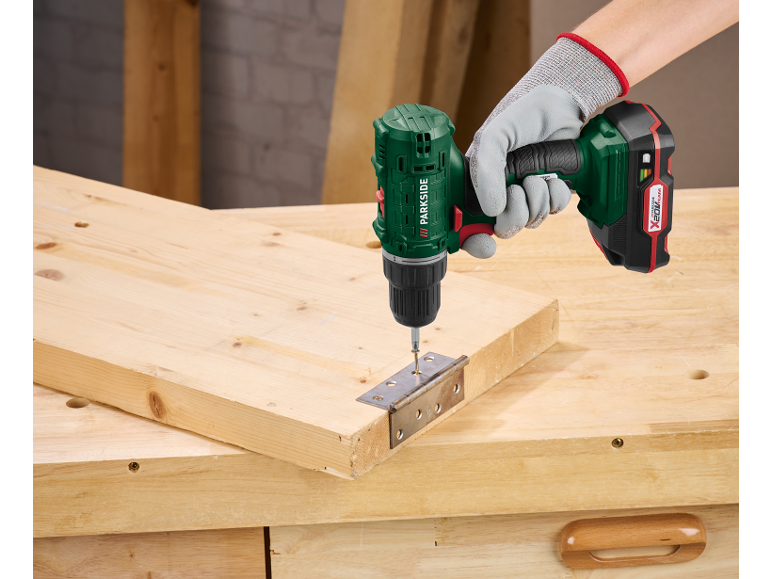 Un trapano avvitatore a batteria viene utilizzato per fissare una cerniera a una tavola di legno.