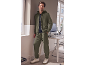 Uomo in tuta verde oliva e sneakers, appoggiato a una parete.
