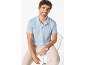 Uomo in polo azzurra e pantaloni beige seduto su una sedia.