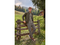 Uomo in giacca bomber color kaki, maglietta e pantaloni cargo, appoggiato a una staccionata di legno.