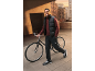 Uomo con gilet imbottito nero, maglia rossa a maniche lunghe e pantaloni cargo neri con bicicletta.
