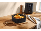 Cesto in silicone nero con crocchette di pollo, anelli di cipolla e patatine fritte, accanto a una friggitrice ad aria.
