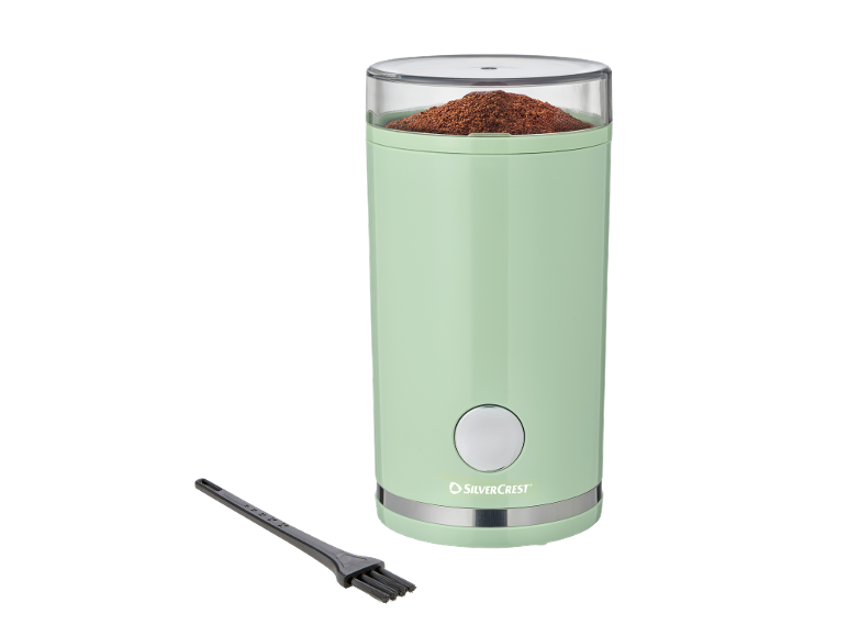 Macinacaffè verde chiaro con caffè macinato e spazzola per la pulizia.