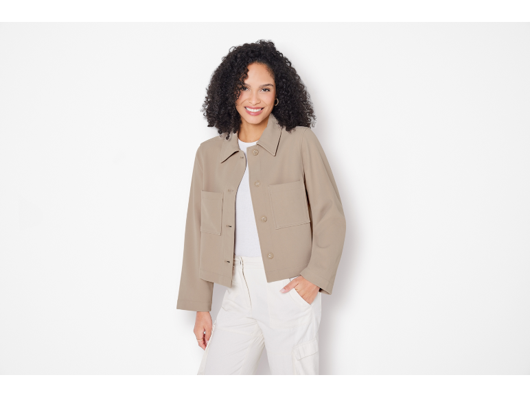Donna sorridente con giacca beige, top e pantaloni bianchi.