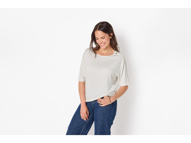 Donna con maglietta color crema a maniche corte e jeans blu, sorridente.