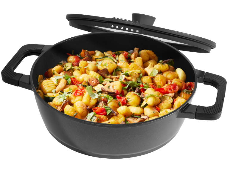 Una pentola nera piena di gnocchi, zucchine, funghi e pomodori, con un coperchio sopra.