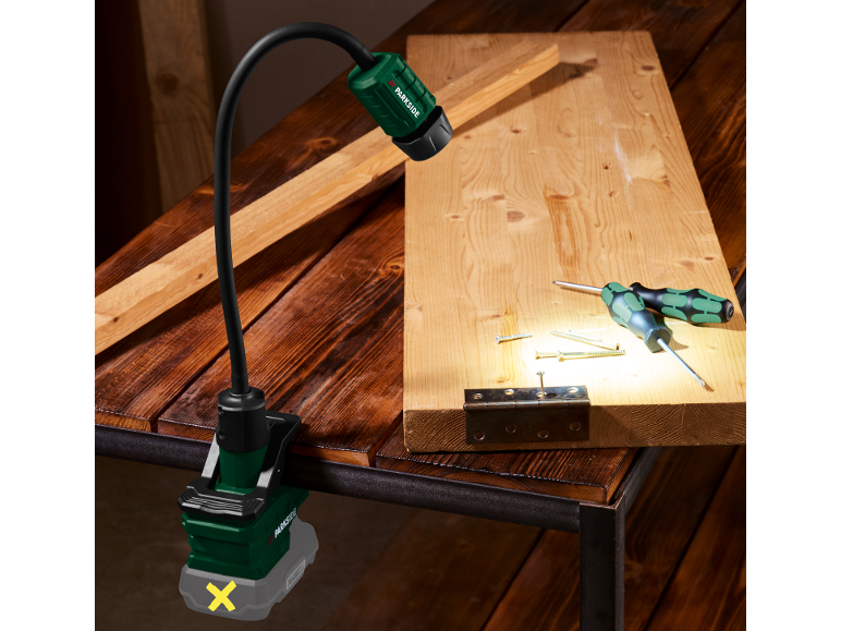 Lampada da lavoro con morsetto illumina una tavola di legno con attrezzi e viti.