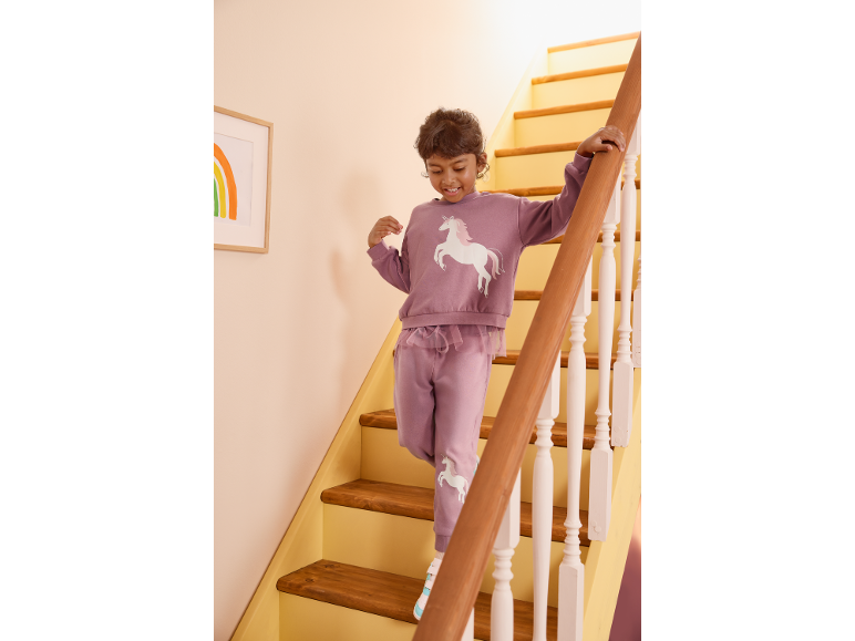 Bambino sorridente in tuta viola con unicorno che scende le scale di legno.