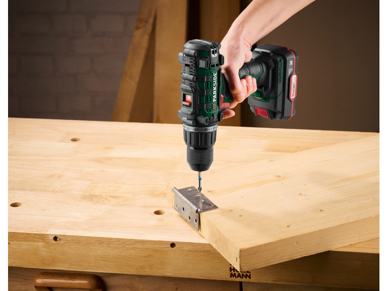 Trapano avvitatore a batteria avvita una vite in una staffa metallica fissata a una tavola di legno su un banco da lavoro.