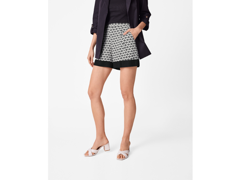 Donna con giacca scura, pantaloncini a fantasia e sandali con tacco basso.