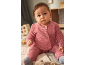 Bambino in completo di maglia rosa, seduto su una coperta.