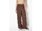 Donna con pantaloni ampi marroni e top corto beige, sandali e bracciale dorato.
