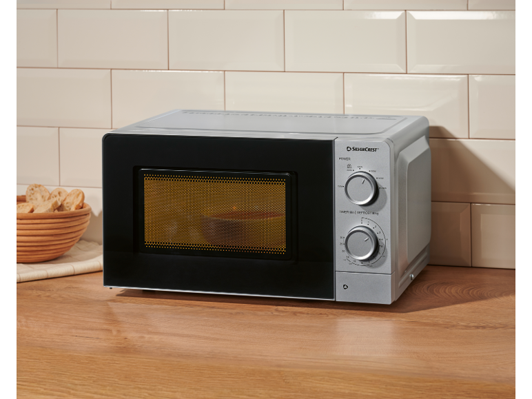 Forno a microonde argentato su un piano di lavoro in legno con un cesto di fette di pane.