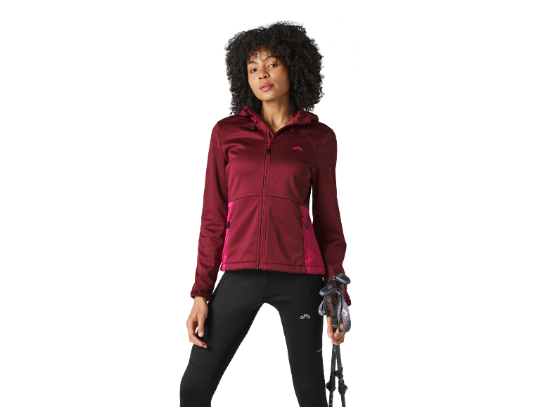 Donna con giacca con cappuccio bordeaux e leggings neri che tiene bastoncini da trekking.