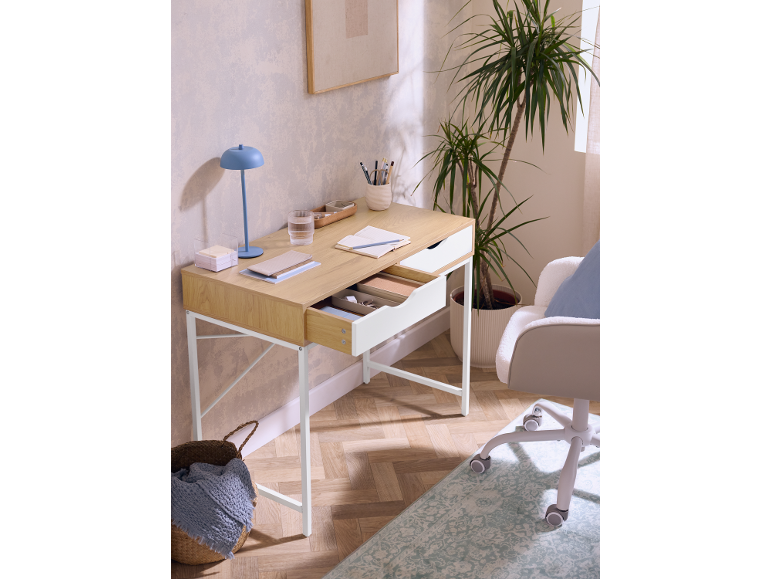Scrivania in legno chiaro con cassetti, lampada blu e pianta in vaso in una stanza moderna.