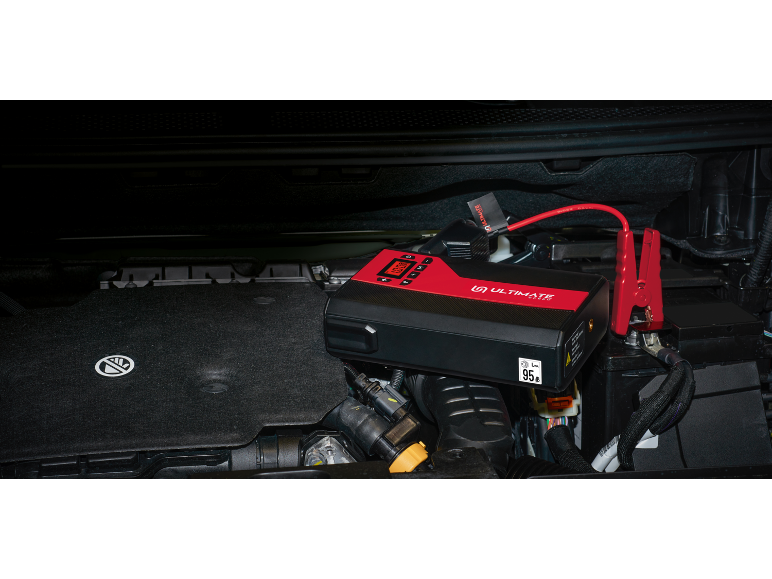 Un avviatore di emergenza portatile rosso e nero collegato a una batteria dell'auto.