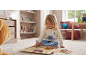 Bambina in pigiama blu e bianco che gioca con un puzzle di legno sul pavimento.