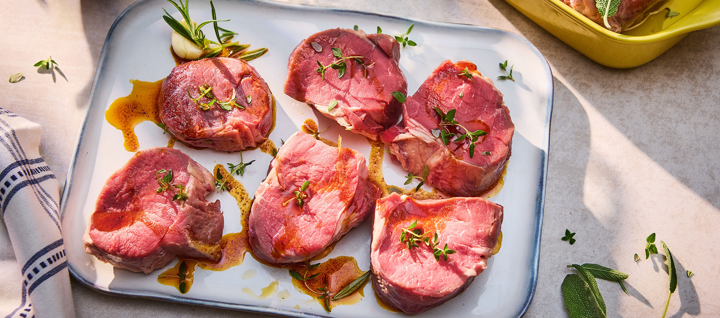 Bistecche di manzo fresche con erbe e olio su un piatto bianco.