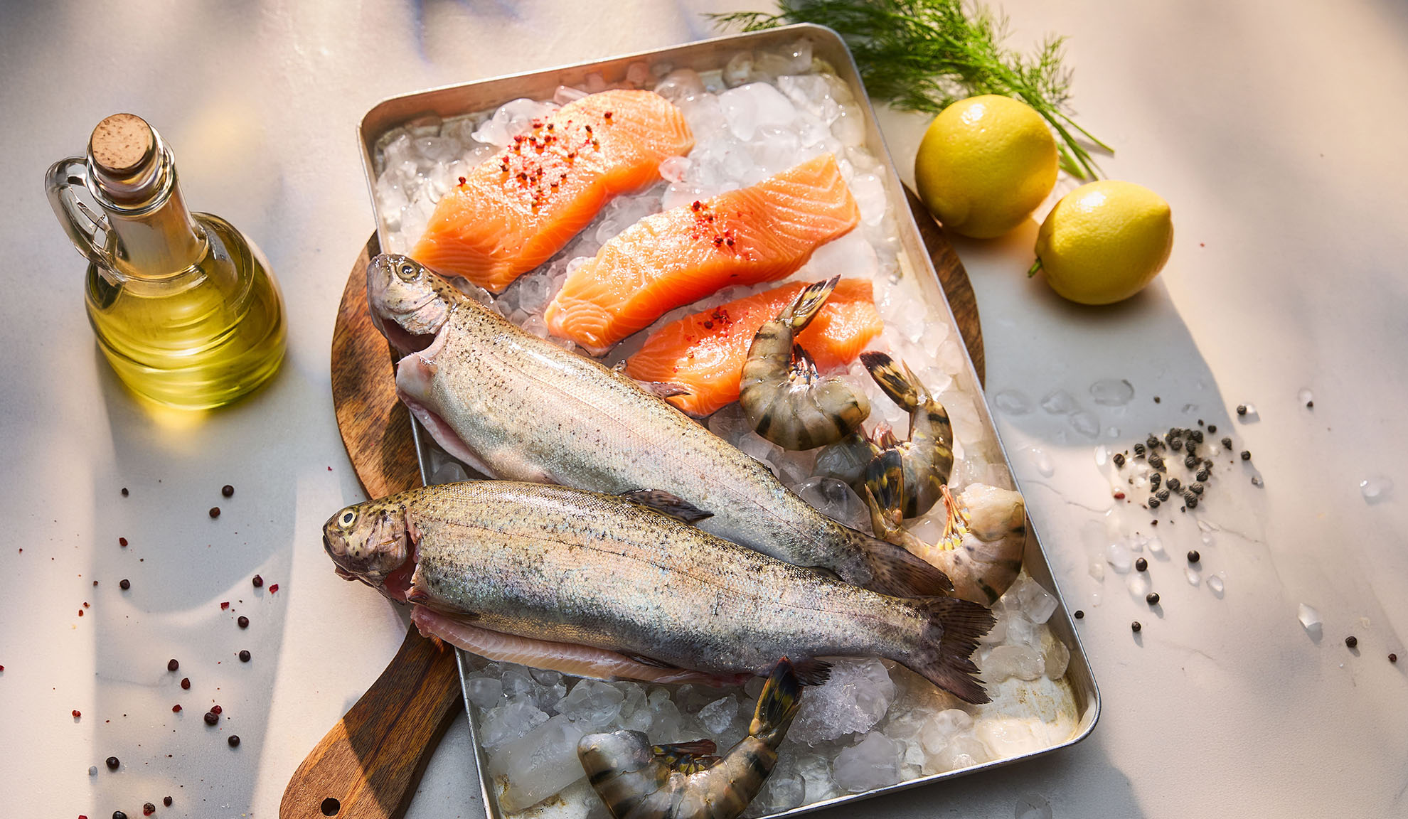 Pesce fresco, filetti di salmone e gamberi su ghiaccio, con limoni e olio.