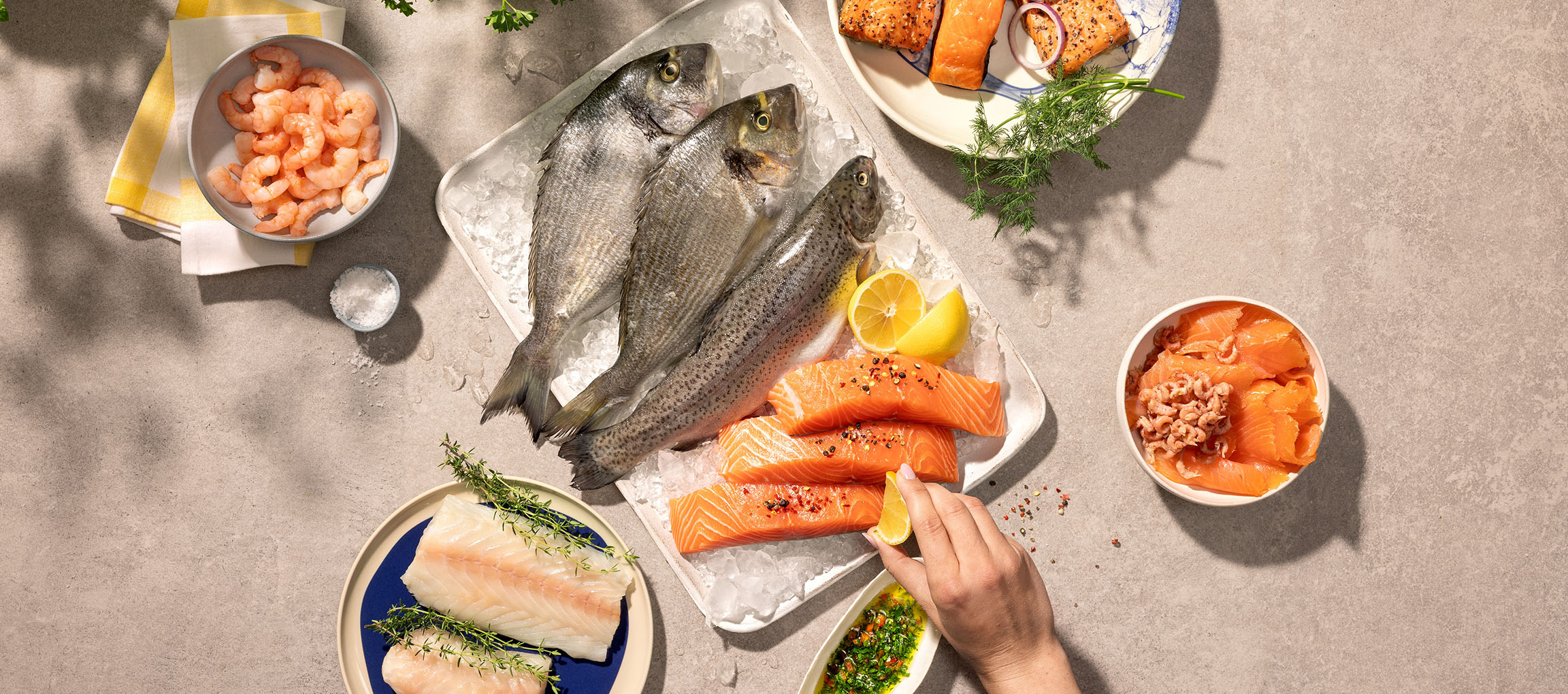 Assortimento di pesce fresco, inclusi pesci interi, filetti di salmone e gamberetti, su ghiaccio.
