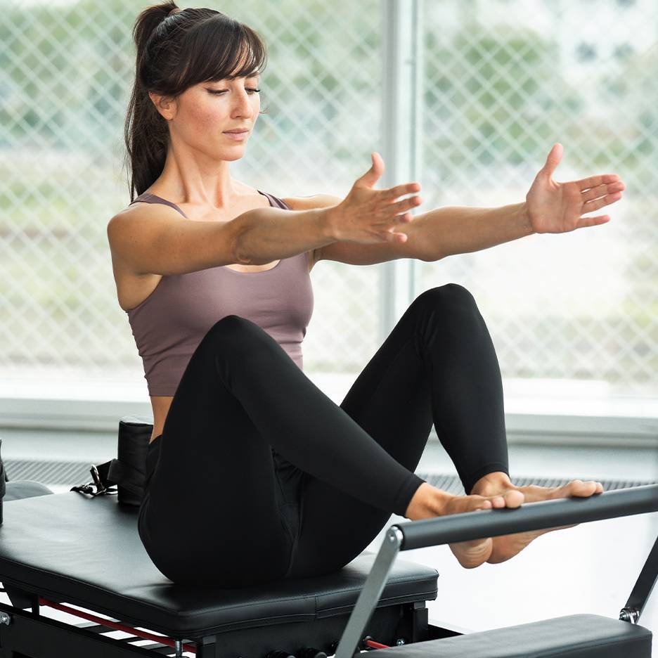 Donna che fa Pilates su un reformer, indossa un top e leggings neri.