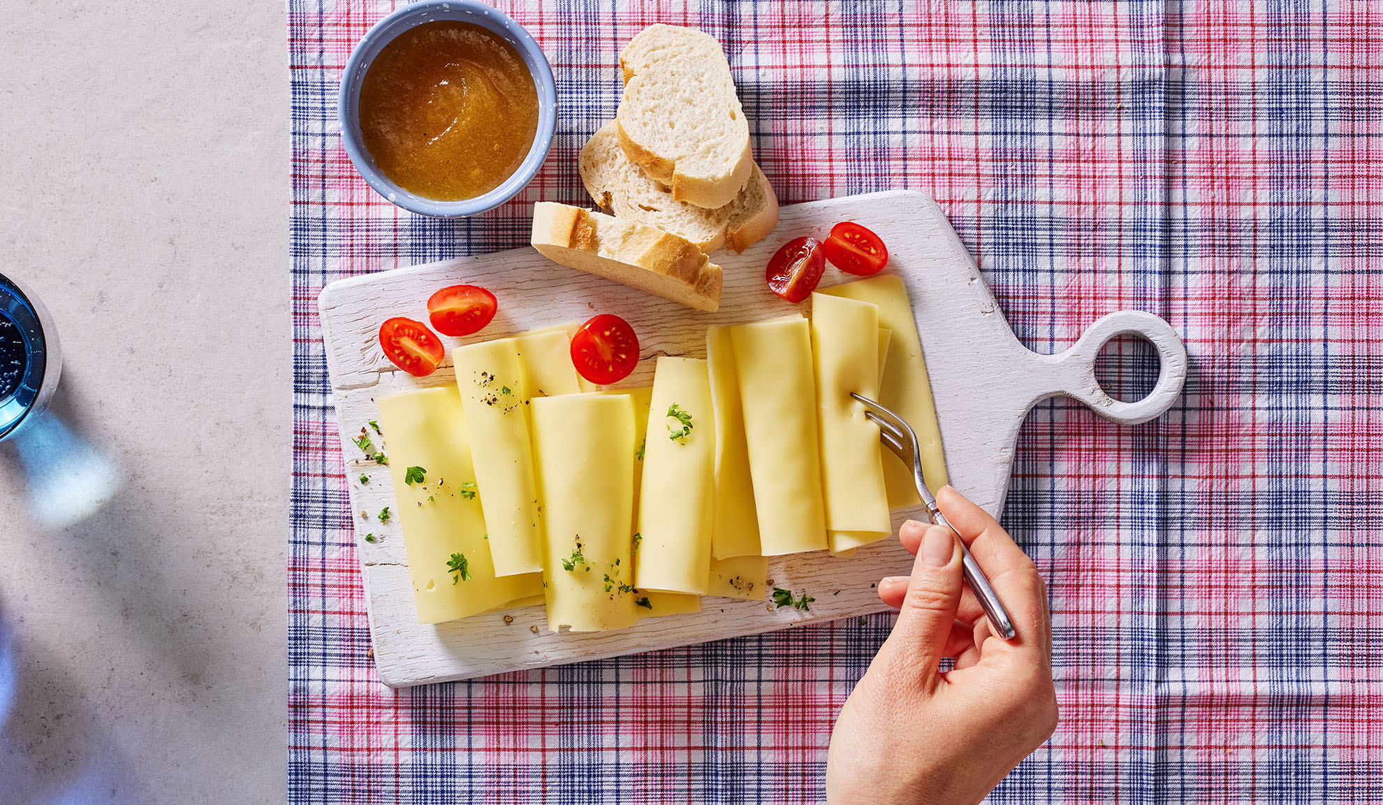 Fette di formaggio, pomodorini, pane e marmellata su un tagliere.