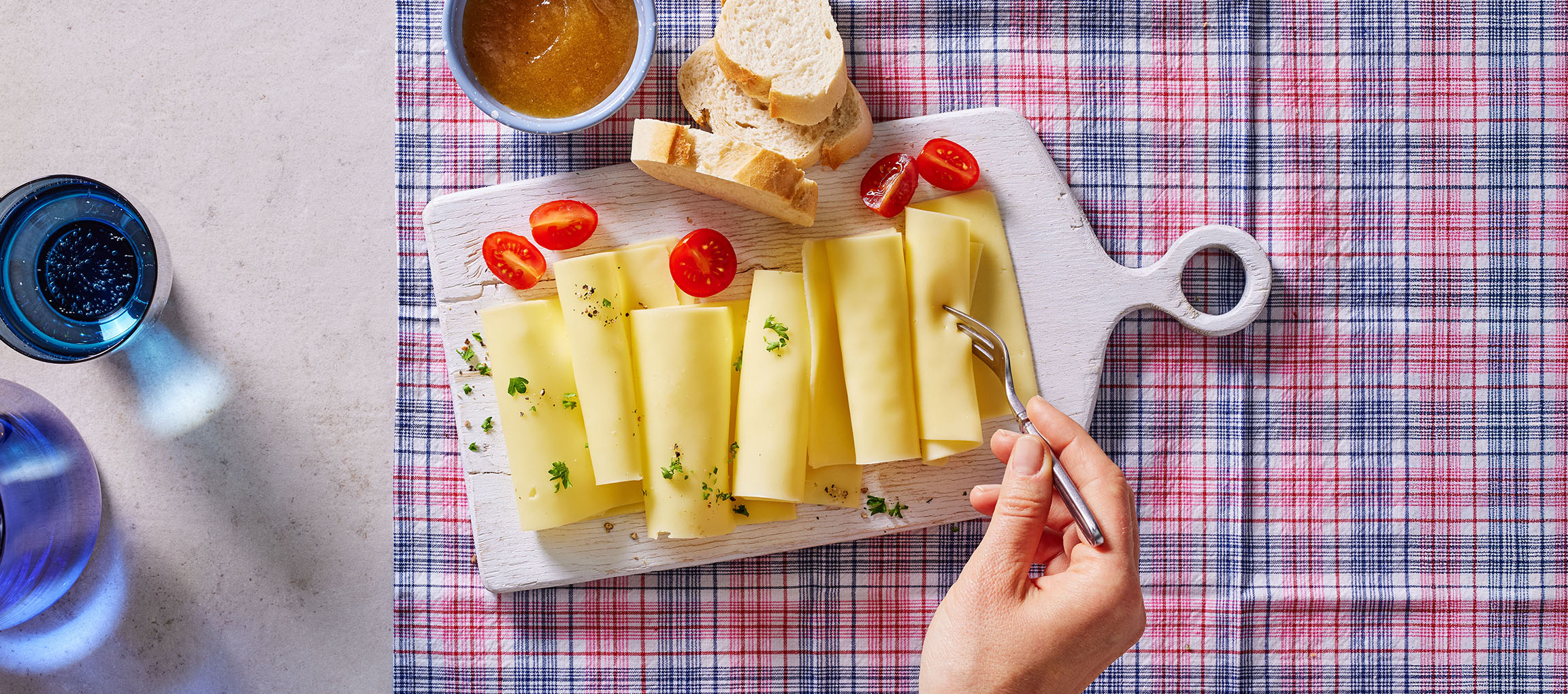 Fette di formaggio con pomodorini, pane e marmellata su una tovaglia a quadri.