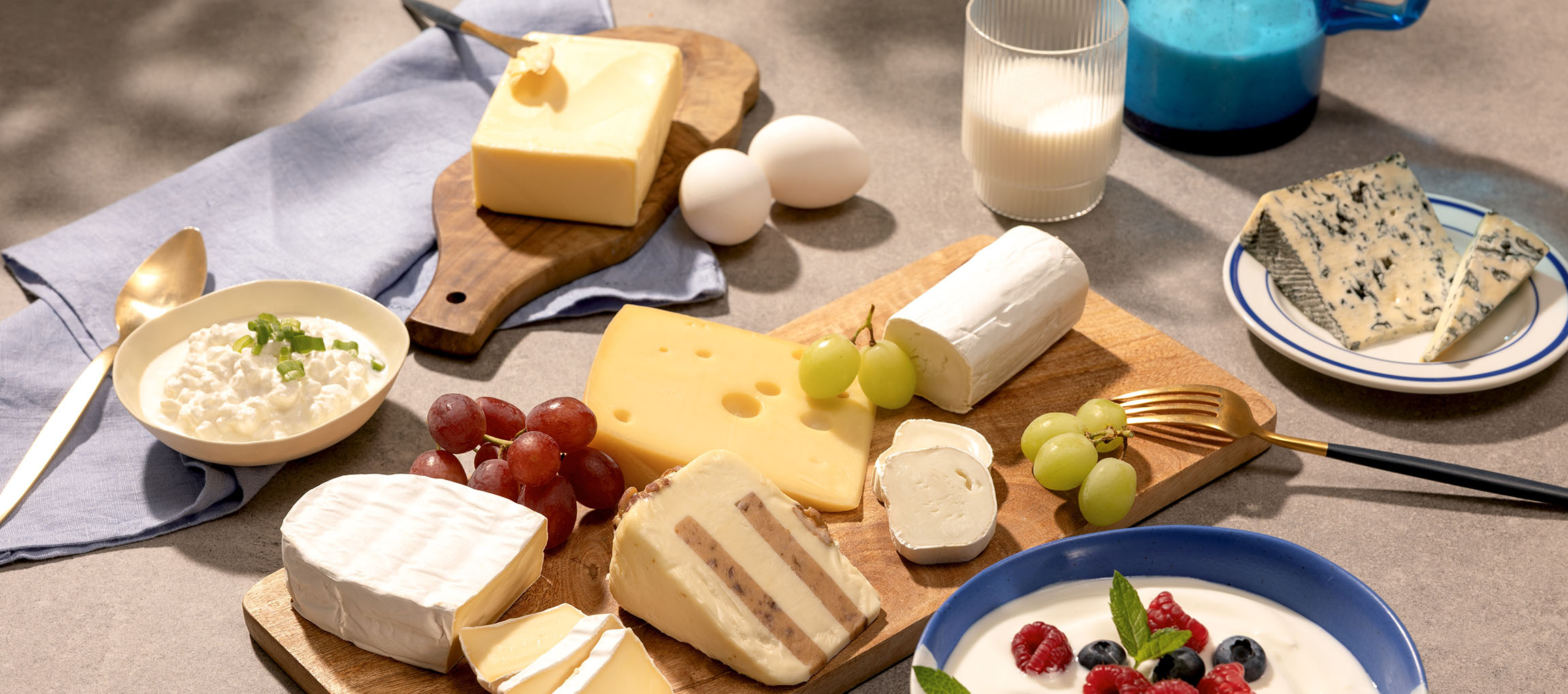 Assortimento di formaggi, uova, uva, latte e yogurt con frutti di bosco su un tavolo.