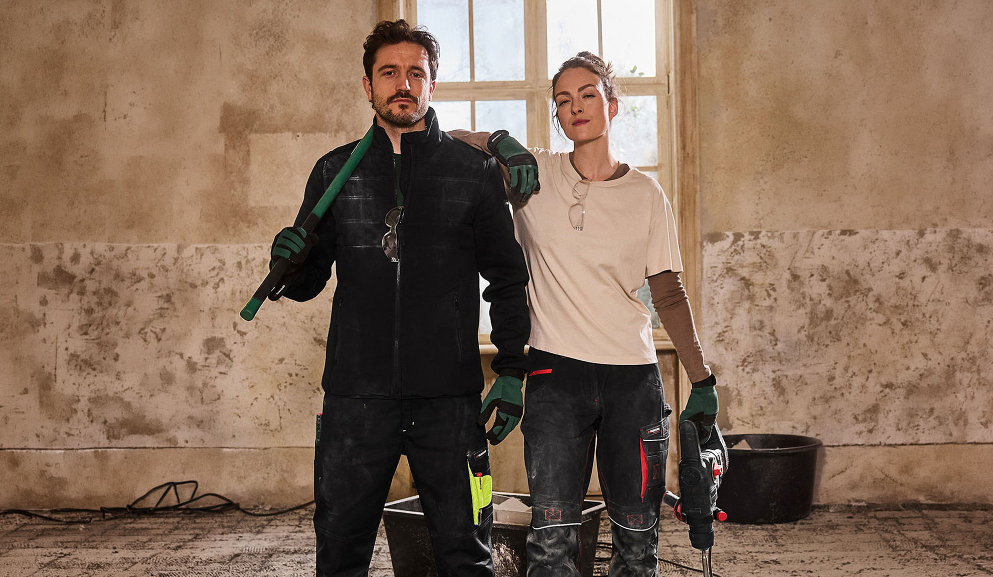 Due operai edili in abbigliamento da lavoro, uomo con pala e donna con trapano.