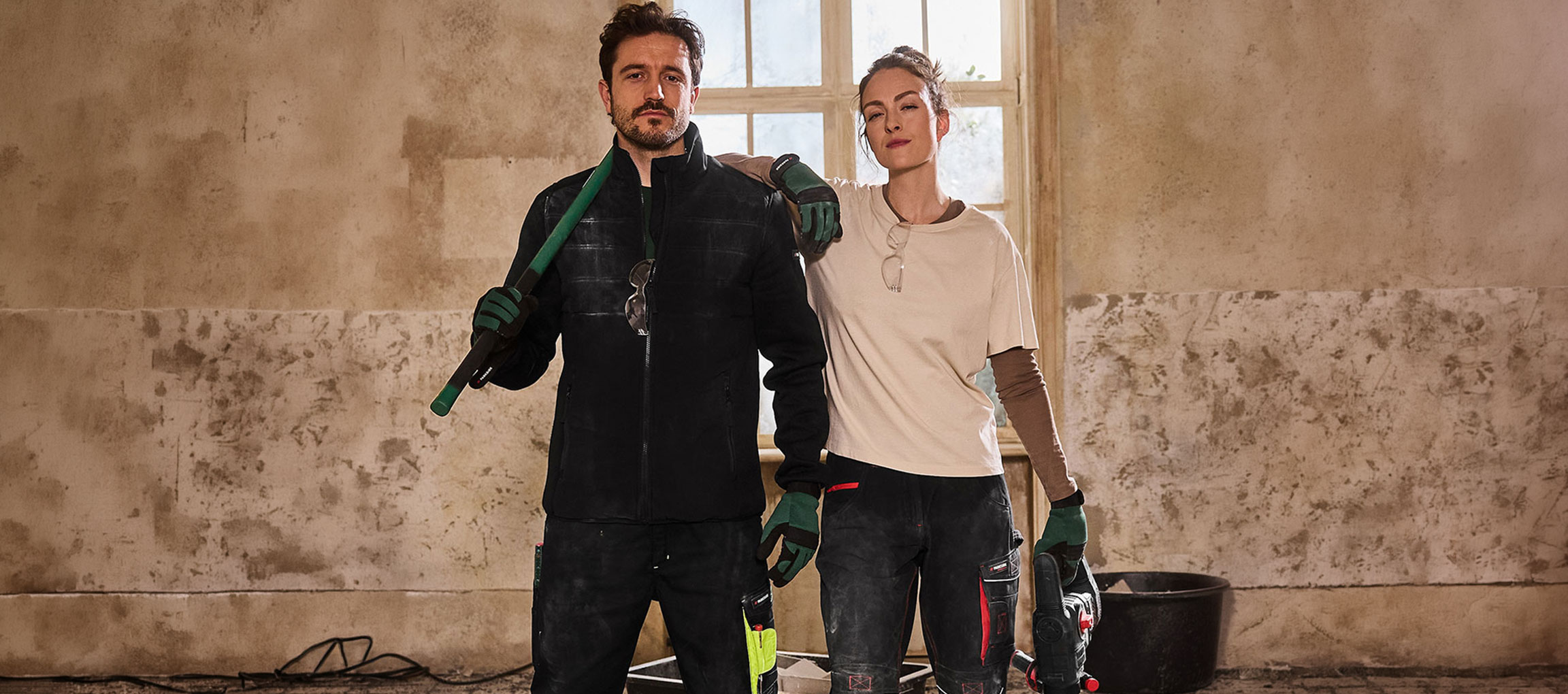 Uomo e donna in abiti da lavoro, con attrezzi, in una stanza in ristrutturazione.