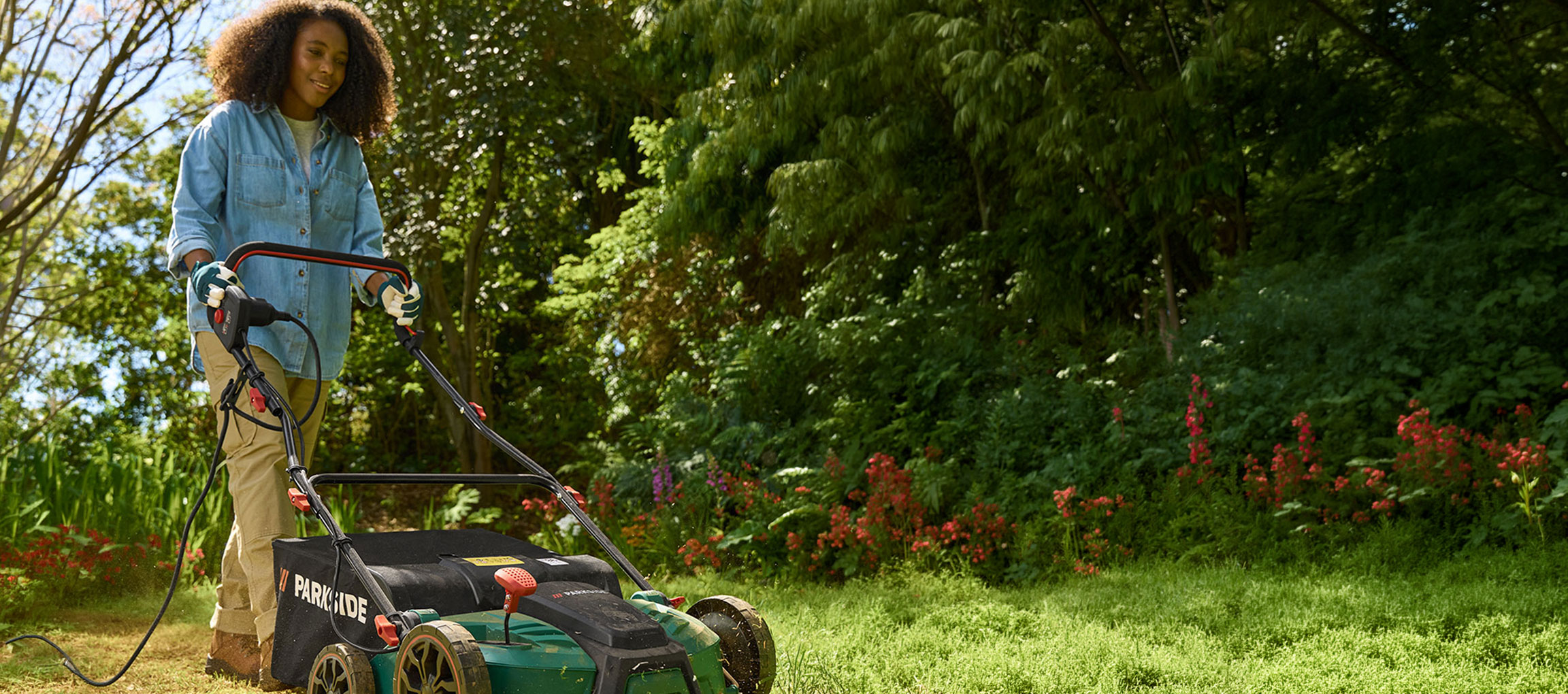 Donna in un giardino che usa un tosaerba elettrico per tagliare l'erba.