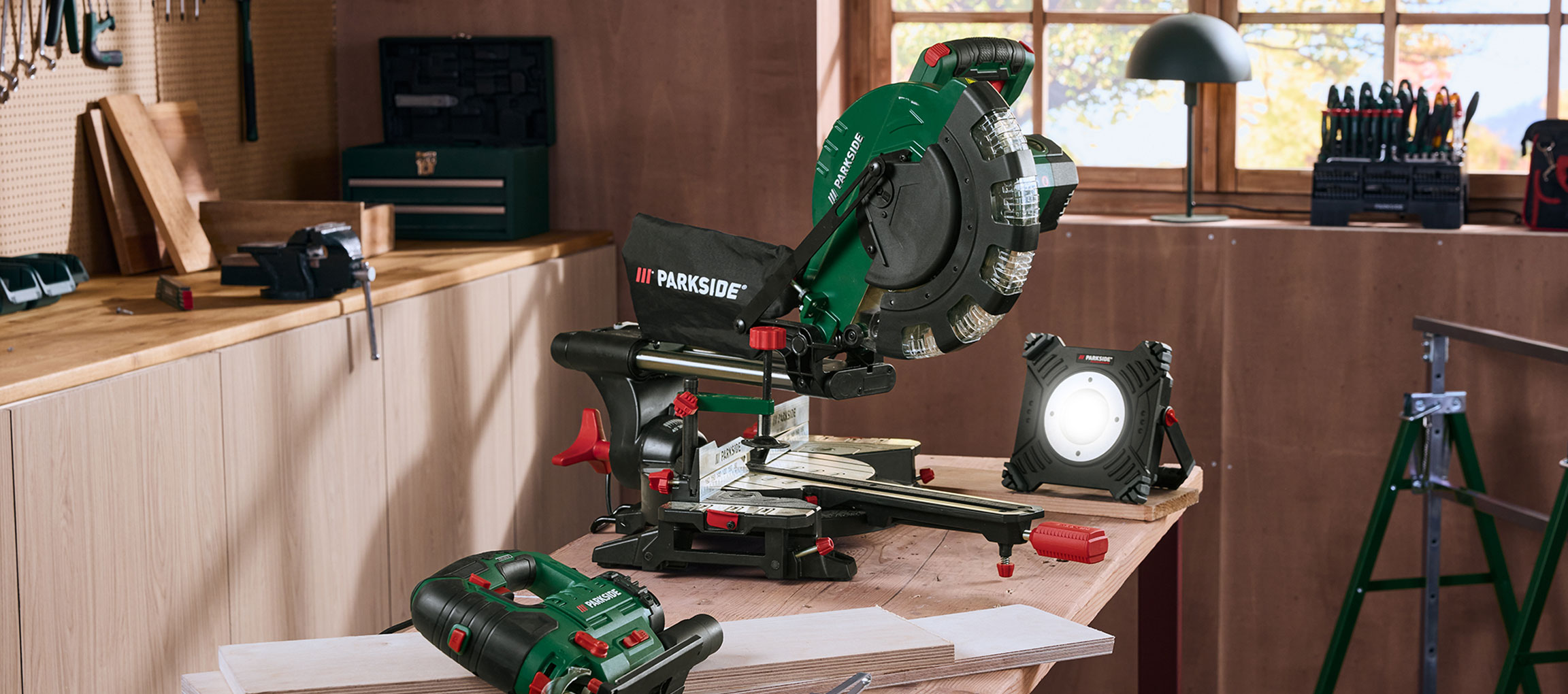 Officina con sega troncatrice, lampada da officina e altri attrezzi su un tavolo di legno.