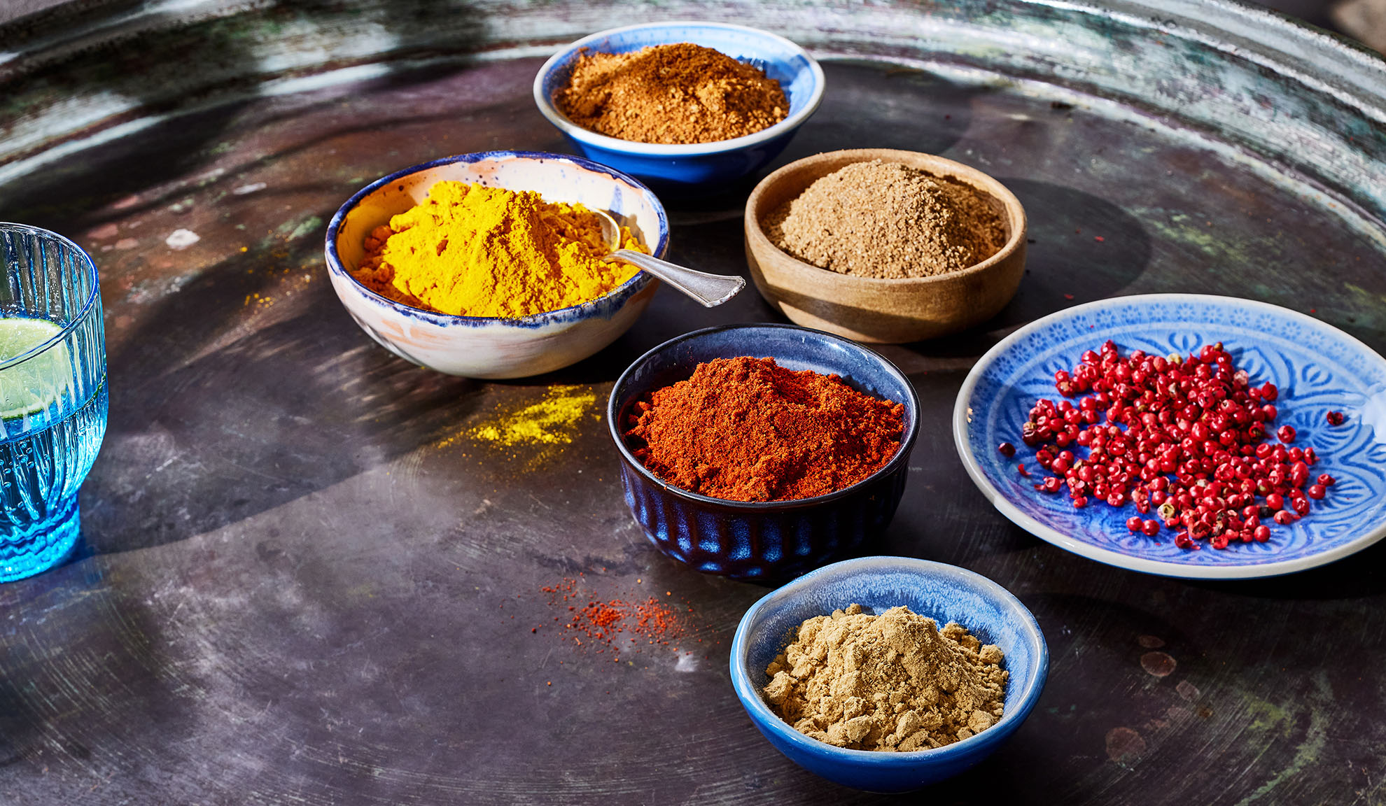 Varie spezie in ciotole: curcuma, paprika, pepe e altre su un vassoio di metallo.