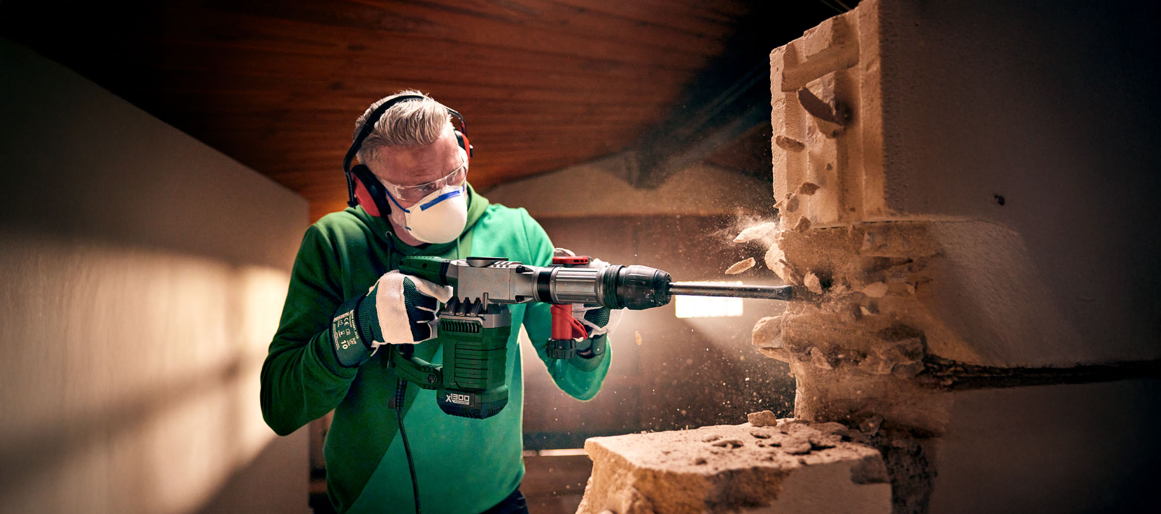 Un uomo usa un martello demolitore Bosch X1300 per demolire un muro di blocchi di cemento.