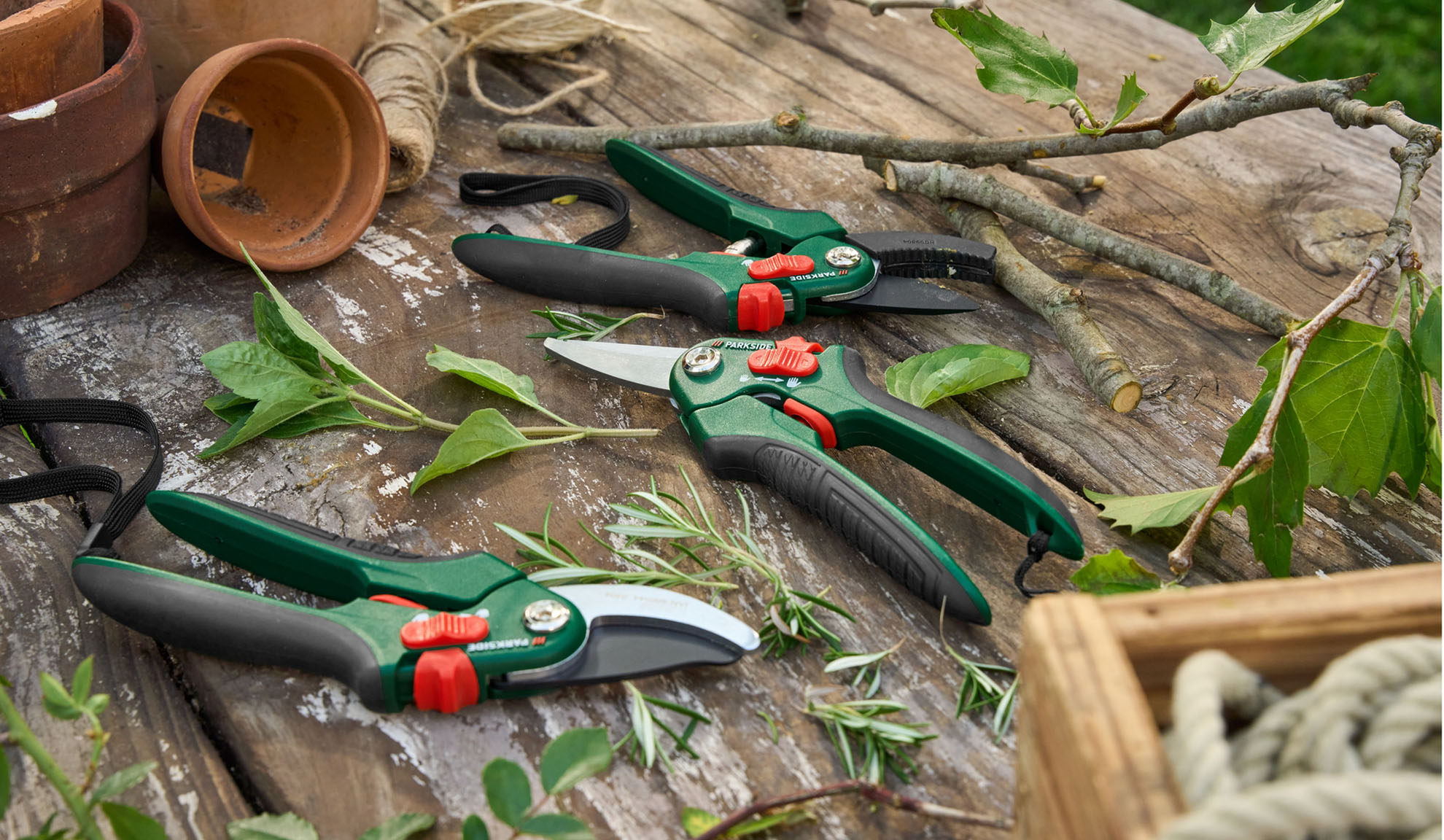Forbici da giardino e cesoie Parkside su una superficie in legno rustica con piante e attrezzi da giardinaggio.