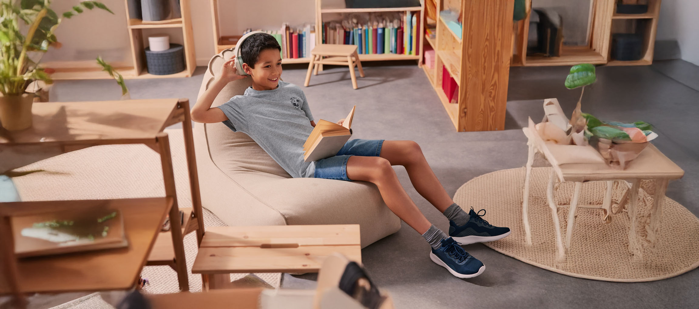 Un ragazzo si rilassa in un pouf, leggendo un libro con le cuffie.