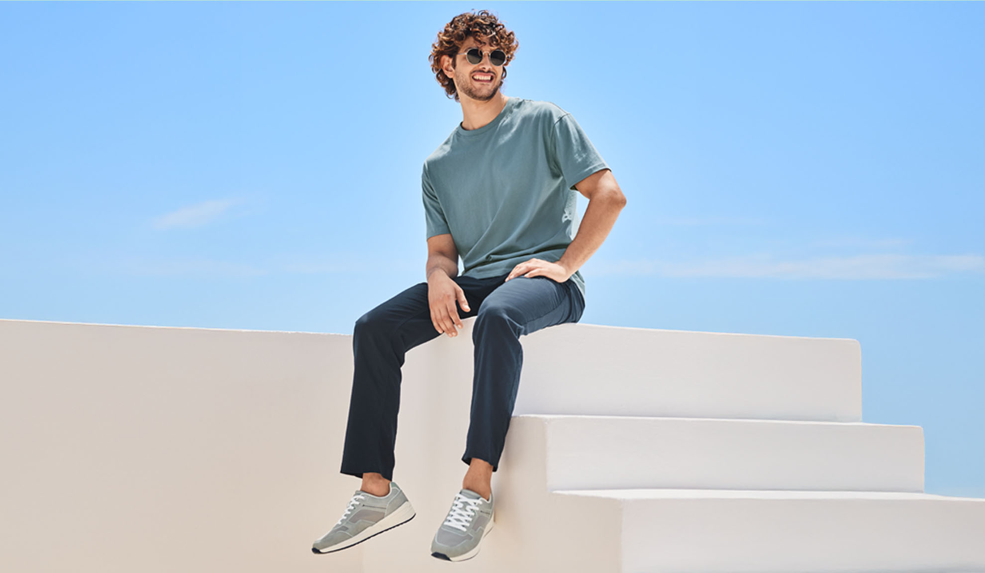 Uomo rilassato che indossa una t-shirt e pantaloni di colore blu scuro, seduto su una scala bianca.