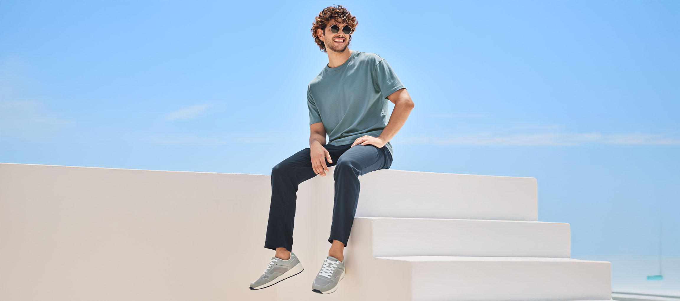 Uomo rilassato che indossa una t-shirt, pantaloni e scarpe New Balance, seduto su una scala bianca.