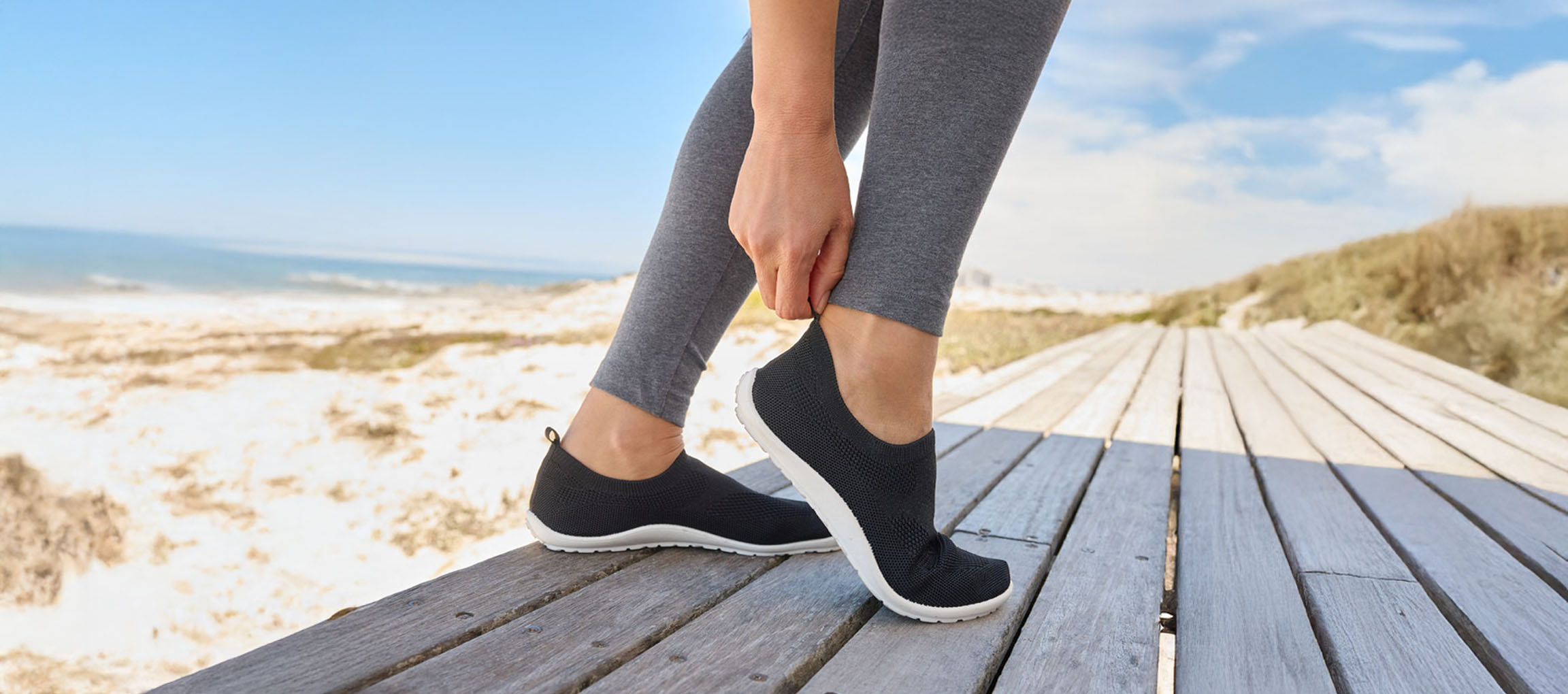 Donna che si allaccia delle scarpe da ginnastica nere vicino al mare.