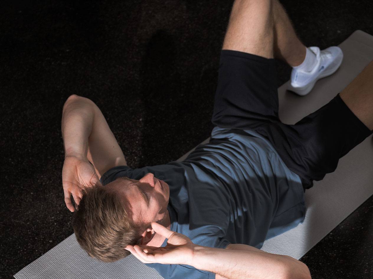 Uomo in maglietta blu e pantaloncini neri fa crunch su un tappetino da yoga.