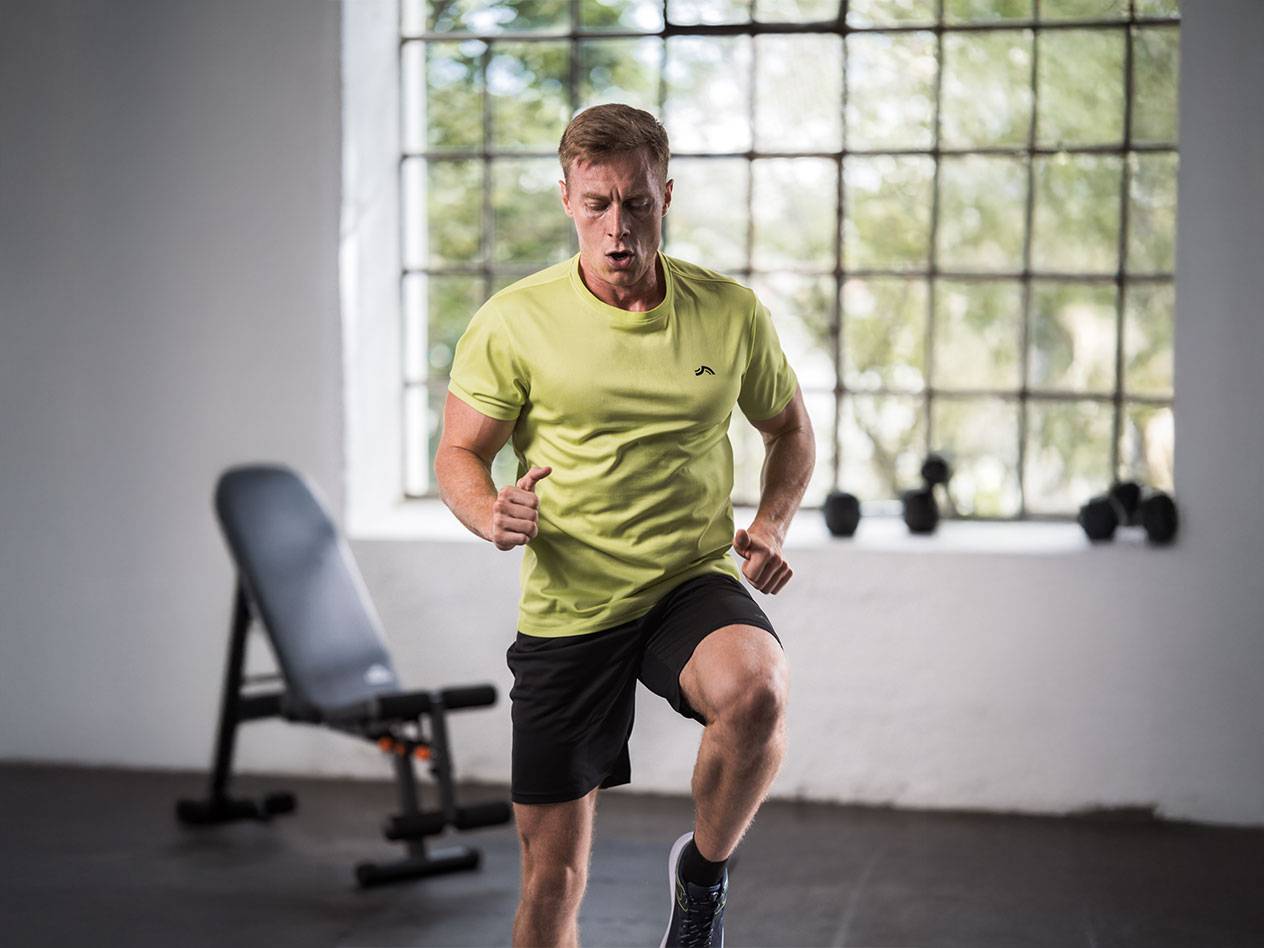 Uomo con maglietta gialla e pantaloncini neri che corre in palestra.