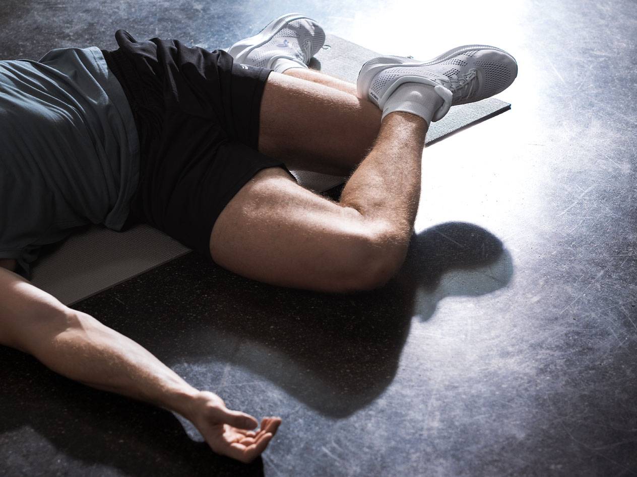 Uomo sdraiato su un tappetino da ginnastica con abbigliamento e scarpe sportive.