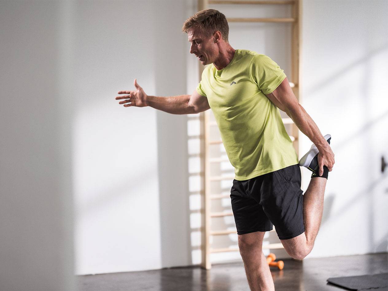 Uomo che si allunga in pantaloncini neri e una maglietta verde lime in palestra.