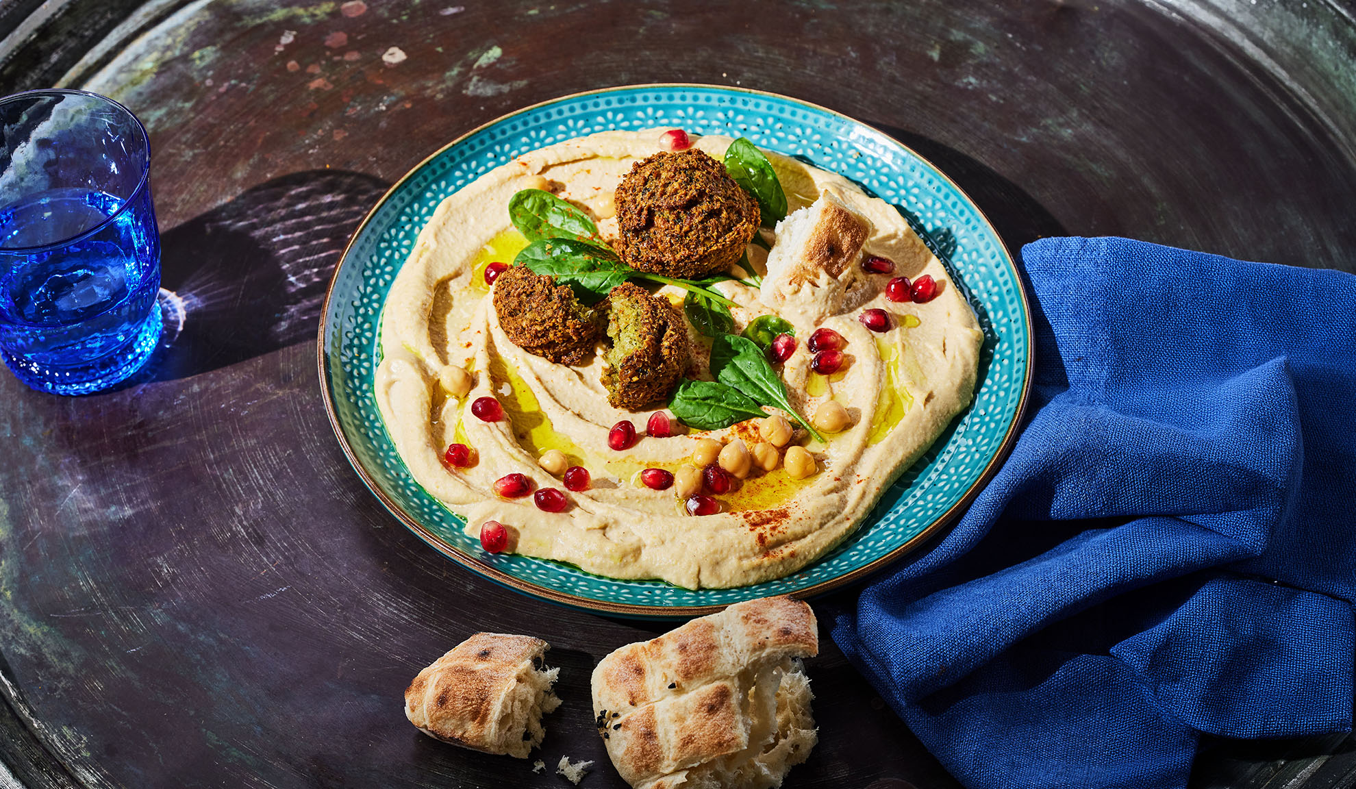Hummus con falafel, semi di melograno e pane pita su un tavolo scuro.