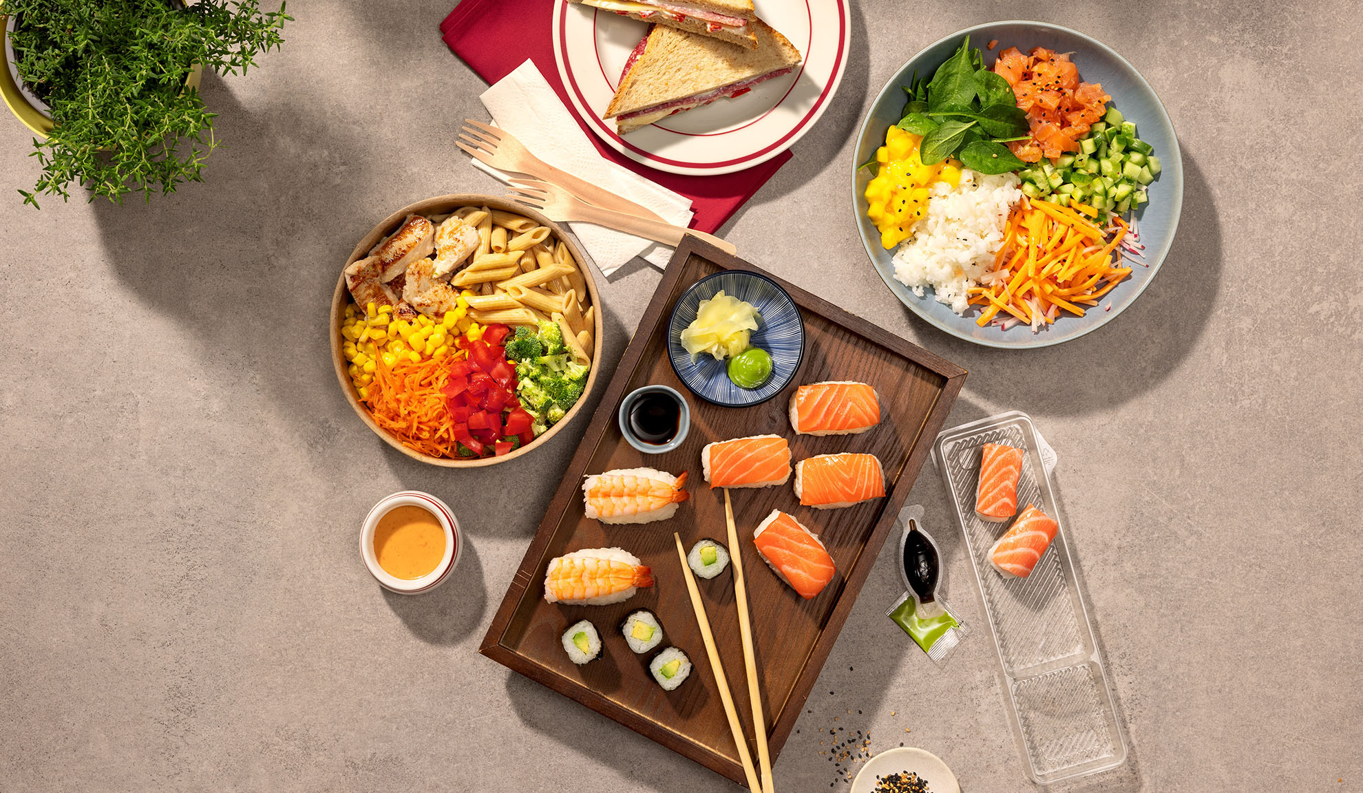 Vista dall'alto di vari pasti da asporto: sushi, poke bowl, insalata di pasta e panini.