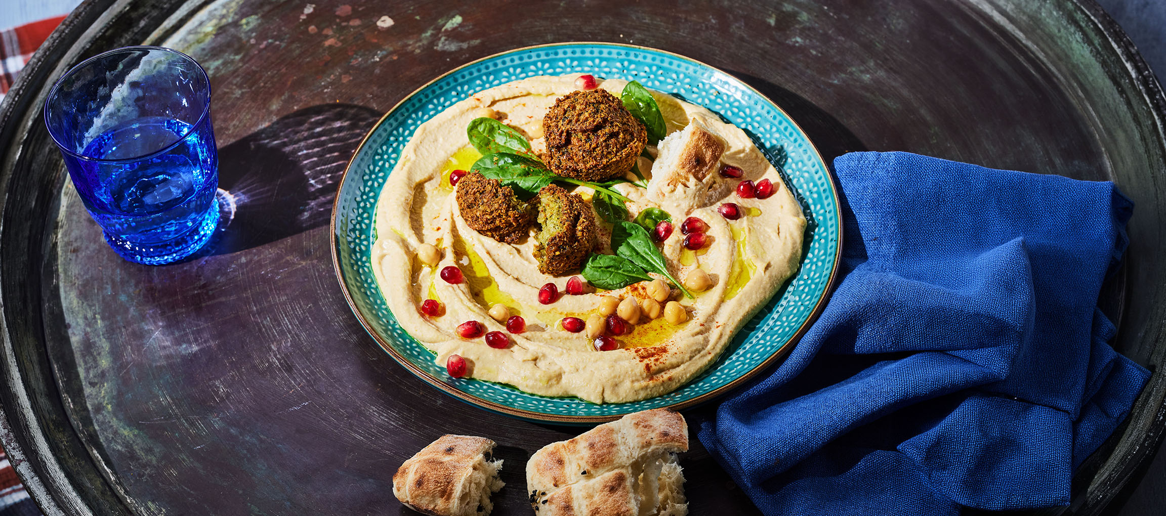 Hummus con falafel, semi di melograno e pane su un vassoio di metallo.