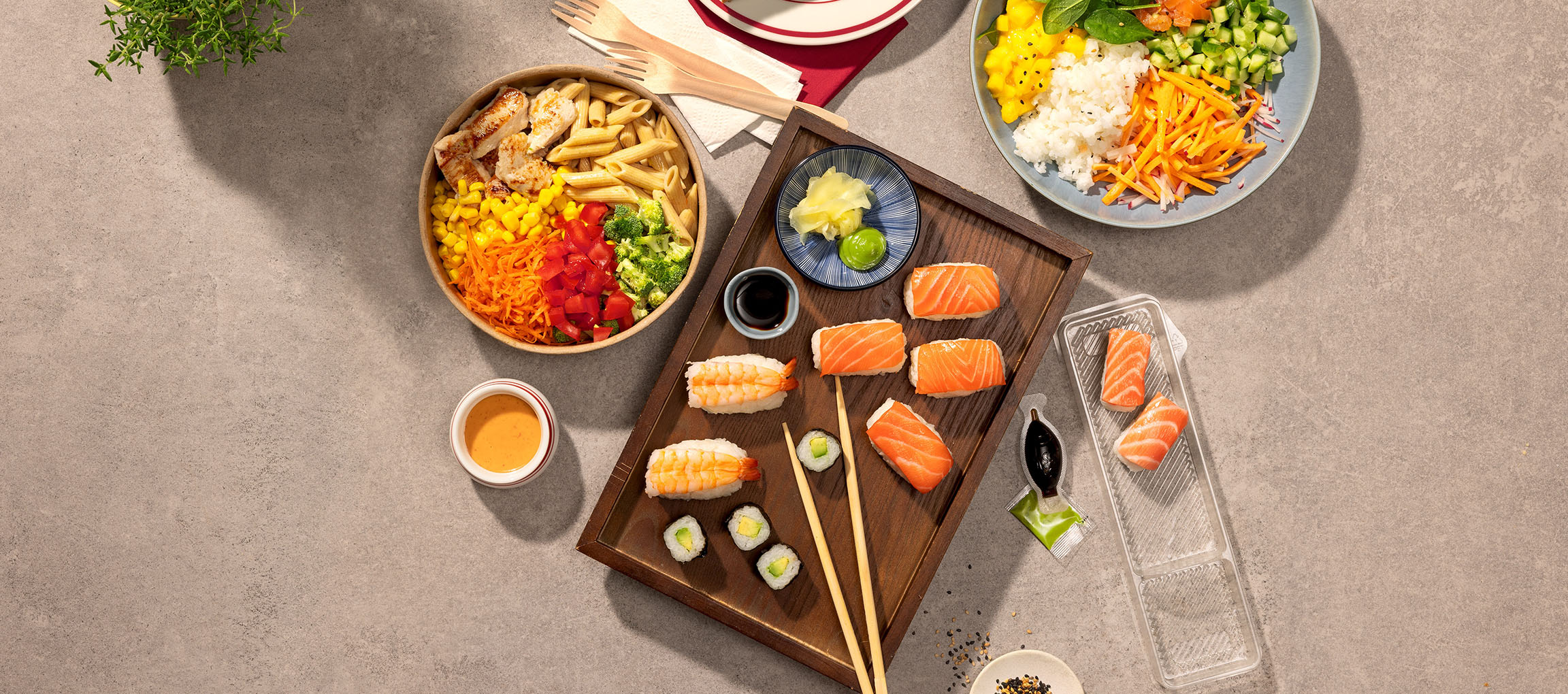 Piatti assortiti: ciotola di pasta e pollo, sushi e una poke bowl su un tavolo.