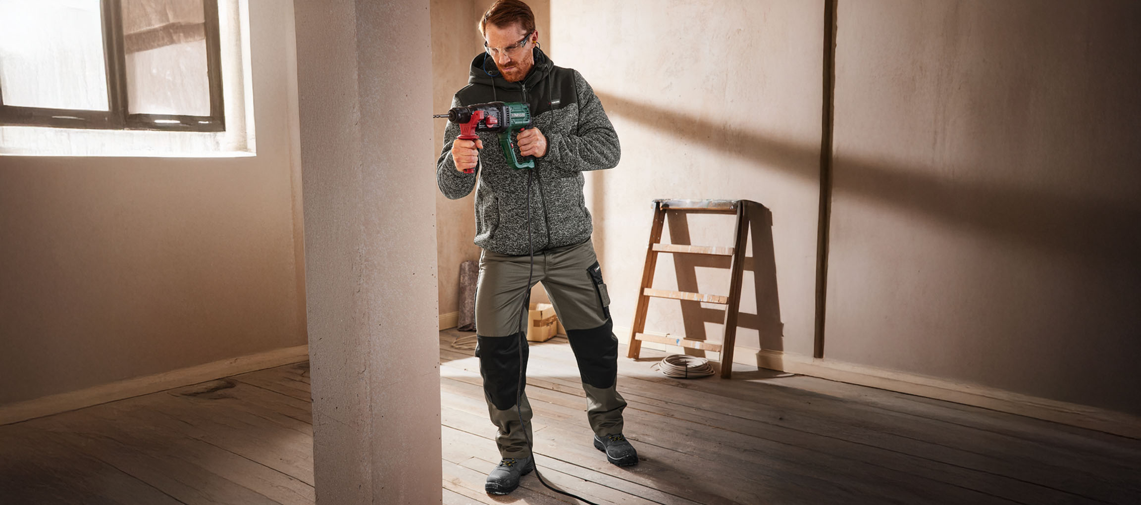 Uomo in abbigliamento da lavoro che fora una parete con un trapano.
