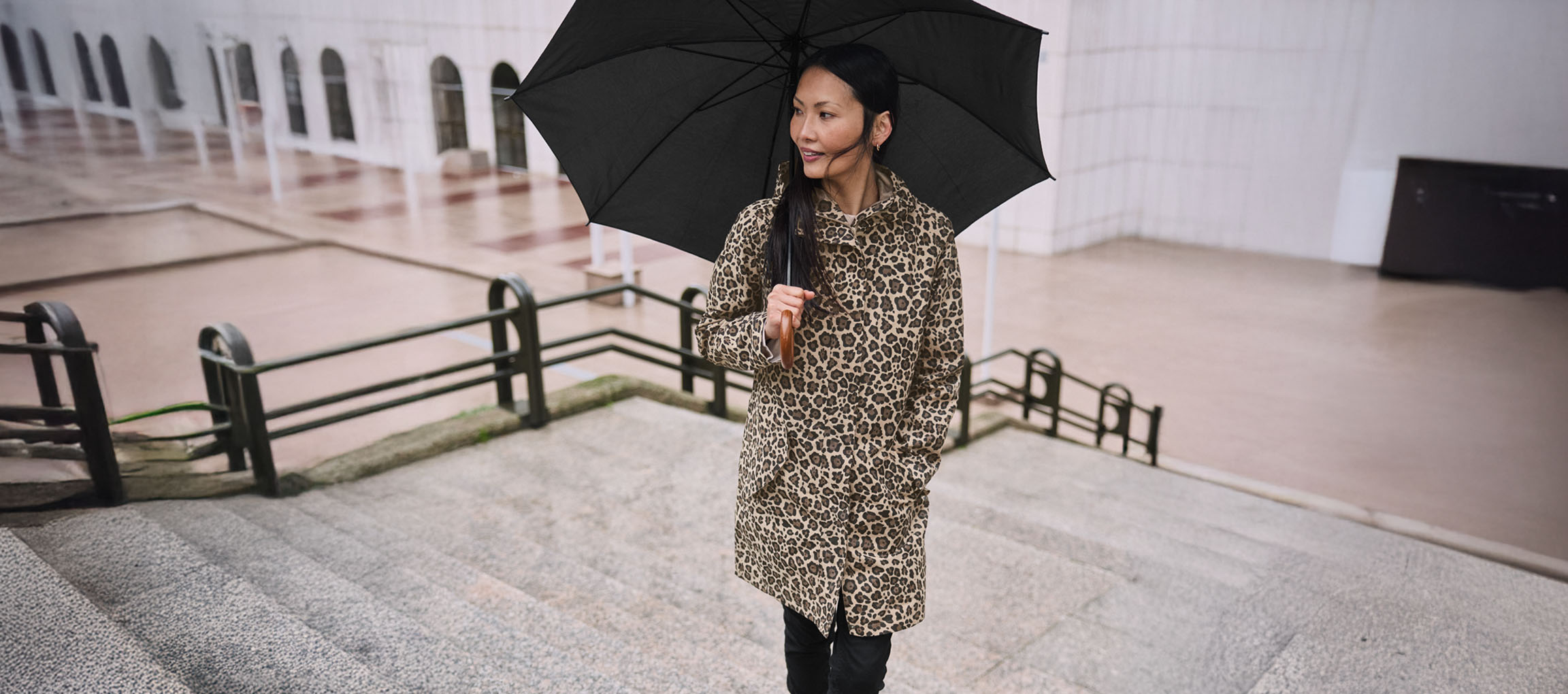 Donna in cappotto leopardato con ombrello sulle scale.