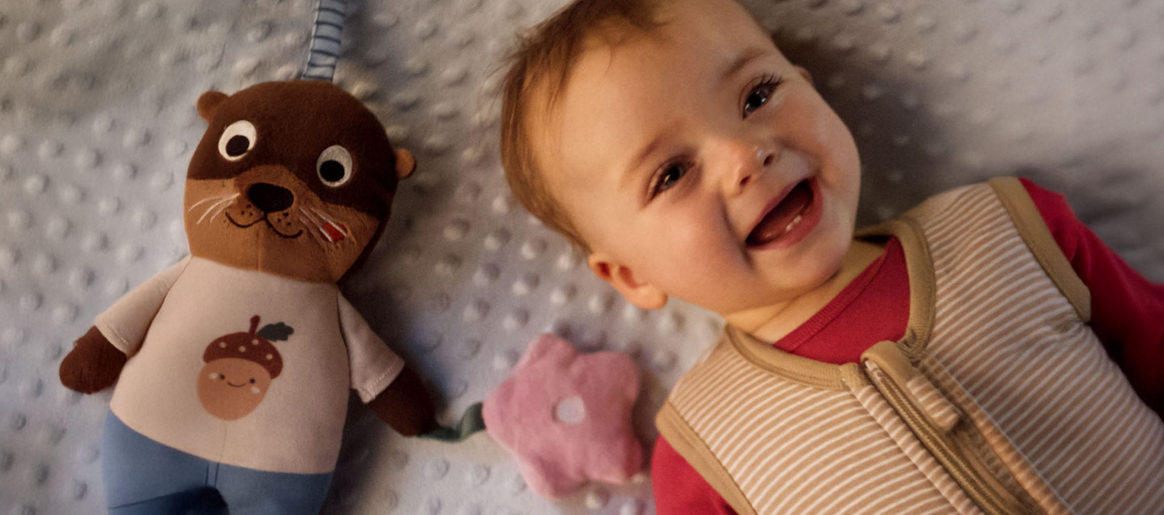 Bambino sorridente e un peluche con una ghianda sulla pancia.